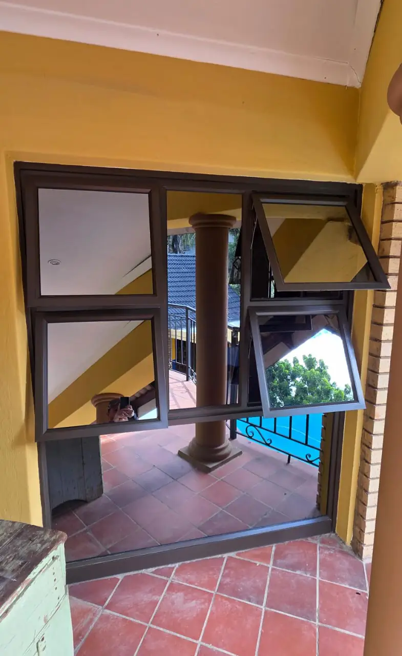 A bronze aluminium unit in the same opening combining fixed glazed panels with two top-hung awning sashes propped open, alongside a doorway onto the tiled patio.